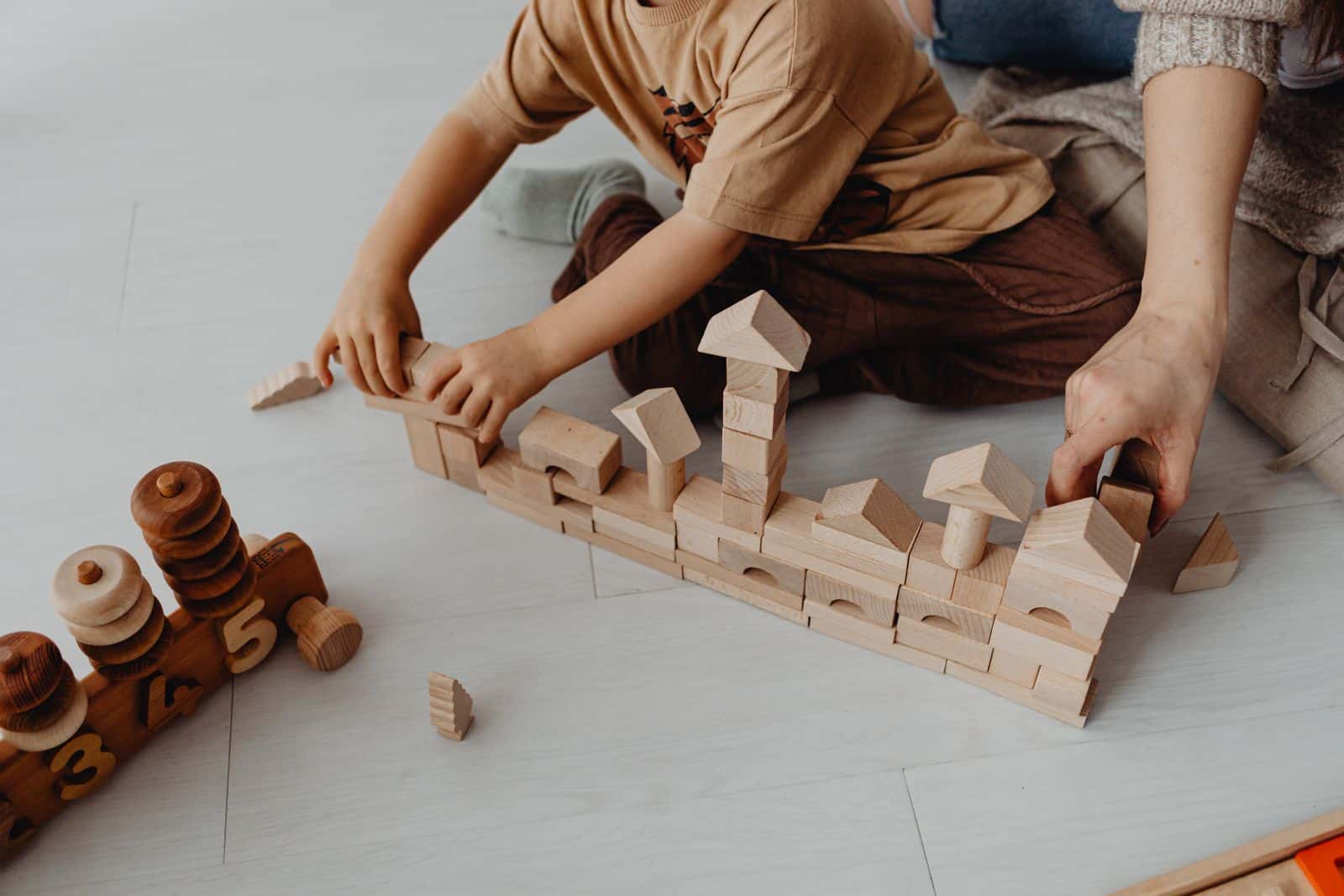 Un enfant, vu de haut, construit une ville en cubes de bois sur le sol avec un adulte