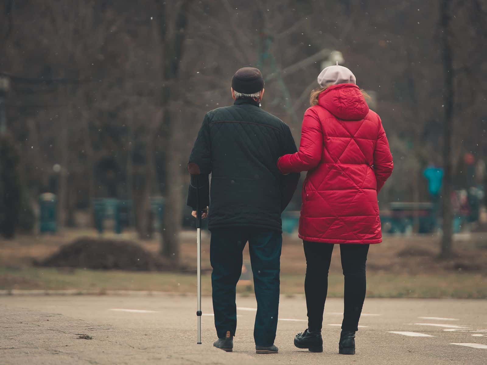 Un couple âgé, vu de dos, marche bras dessus bras dessous dans un parc, l'homme s'appuie sur une canne