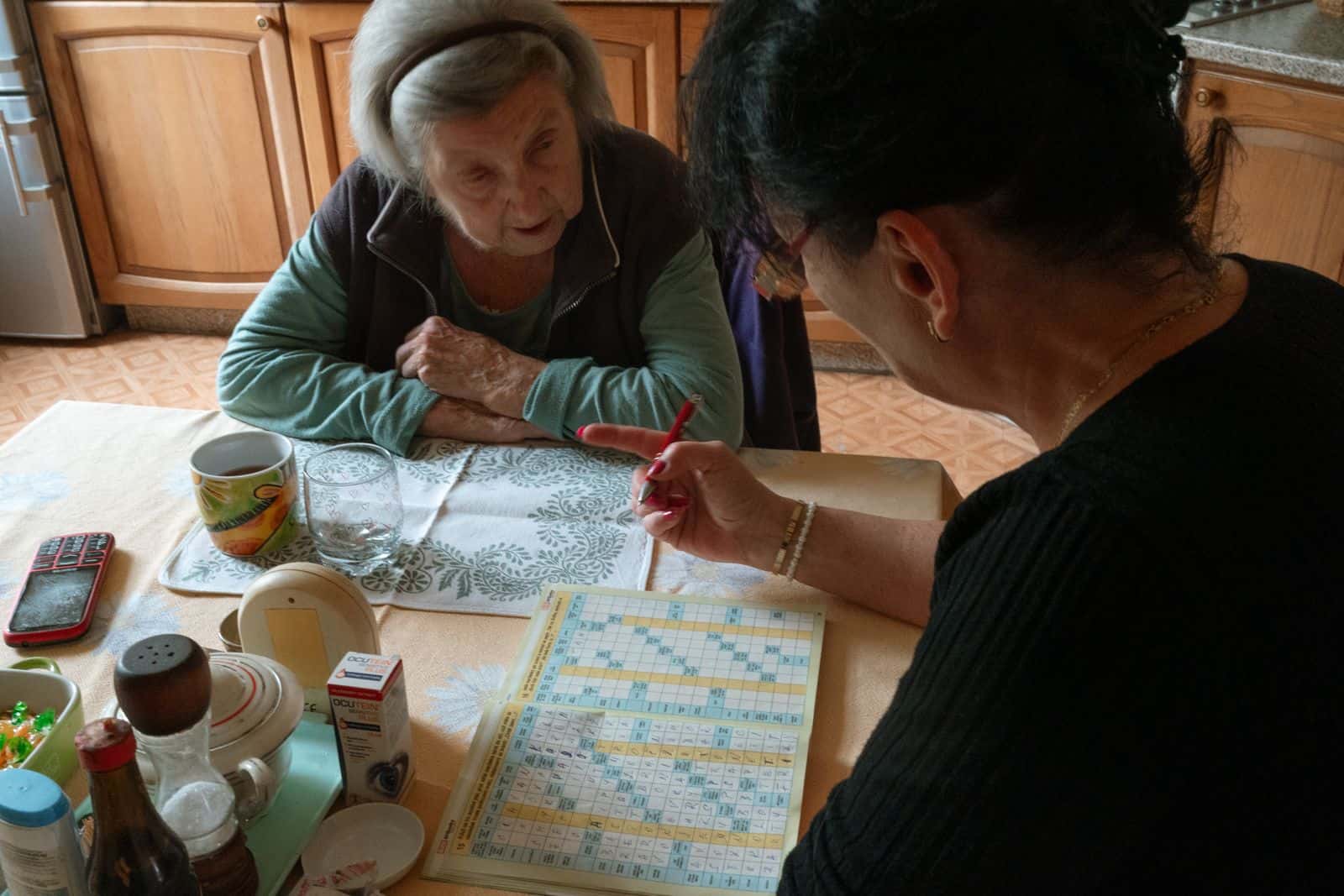 Une femme âgée et une femme plus jeune remplissent une grille de mots croisés à une table de cuisine