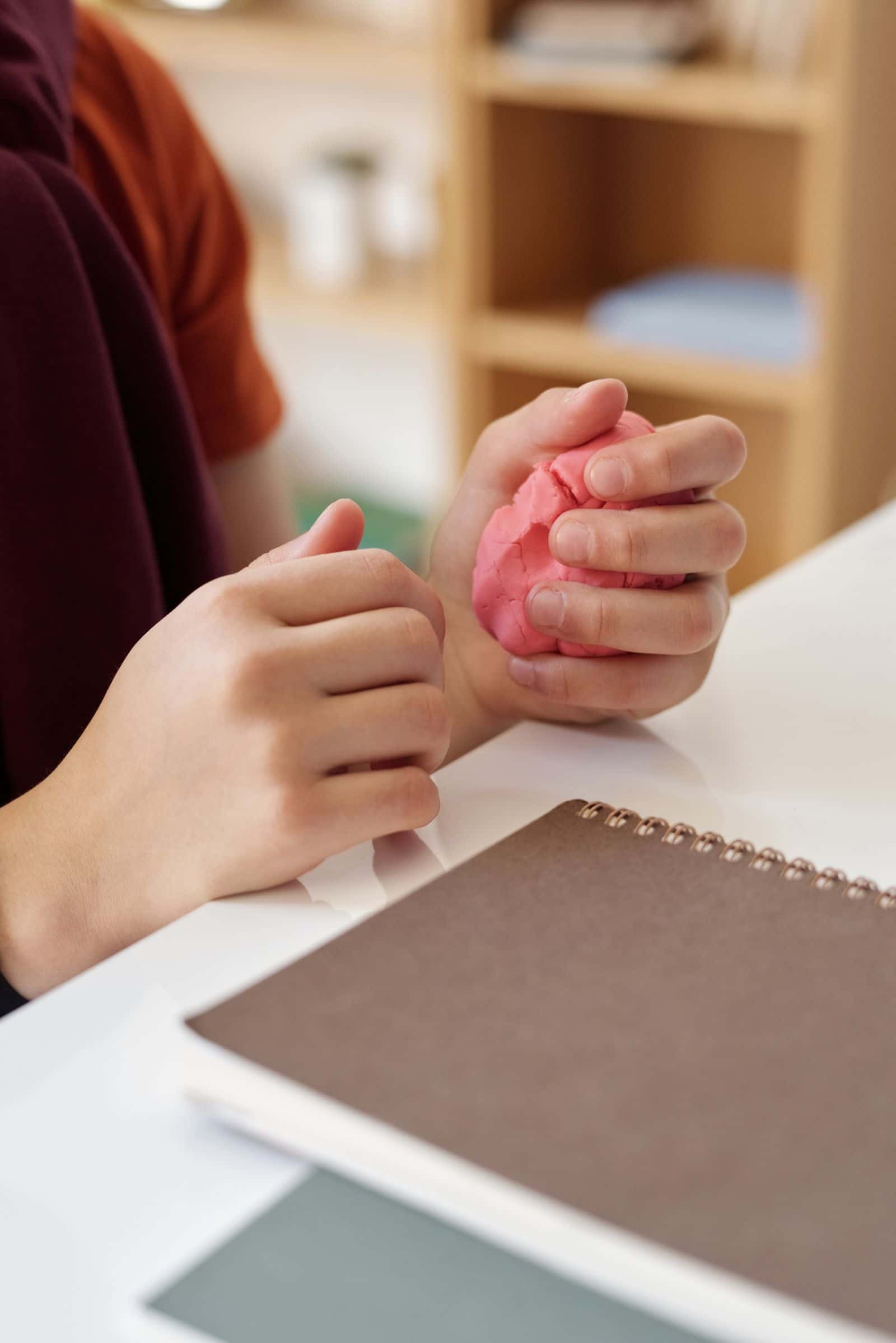 Les mains d'une adolescente modèlent de la pâte rose sur un bureau