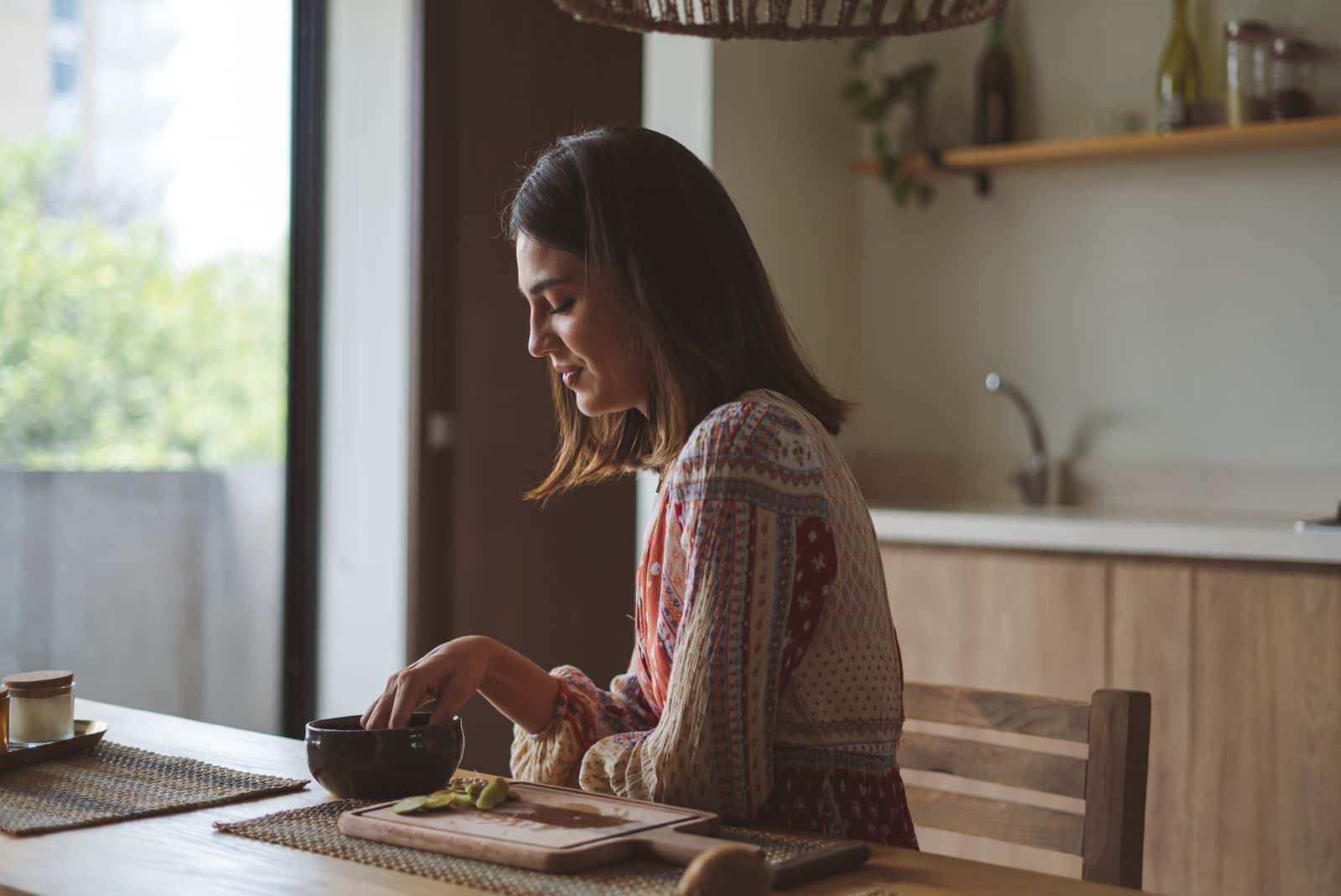 Une femme d'une quarantaine d'années prend un repas à une table de cuisine, près d'une fenêtre