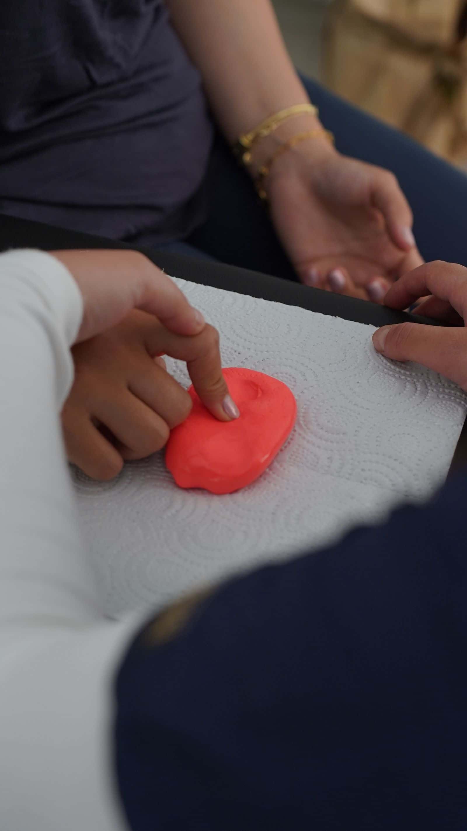 La main d'un adulte guide la main d'un enfant qui presse de la pâte à modeler rouge