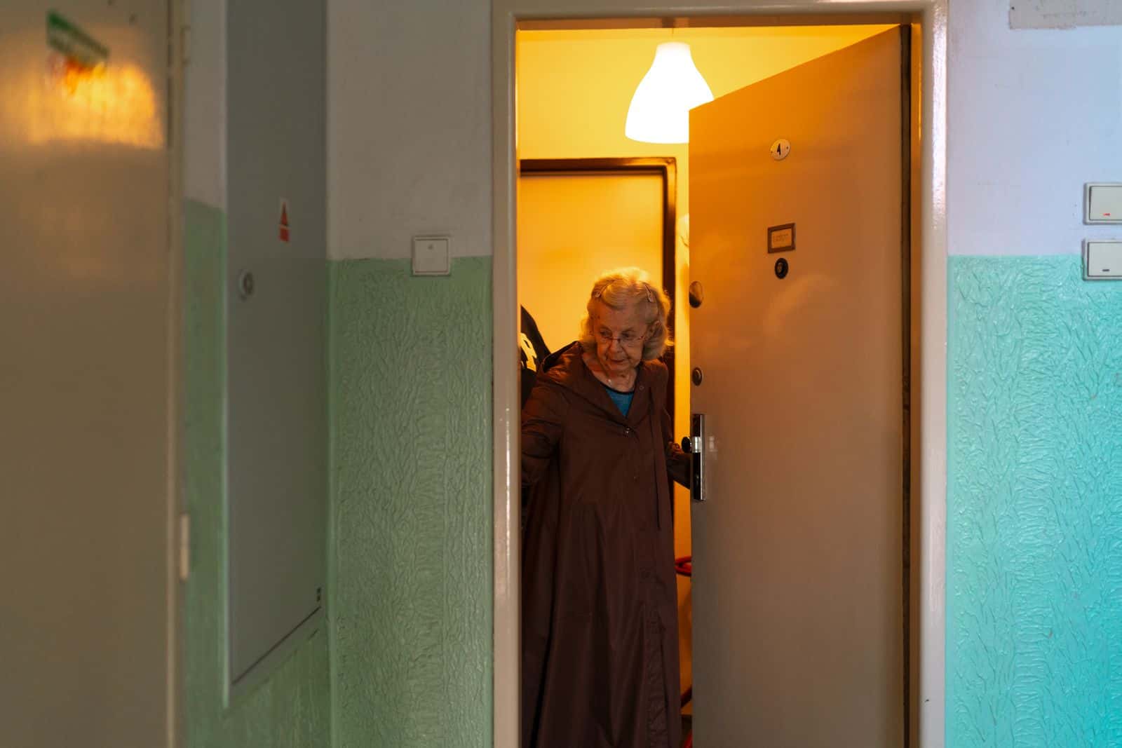 Une femme âgée ouvre la porte de son appartement sur un palier d'immeuble