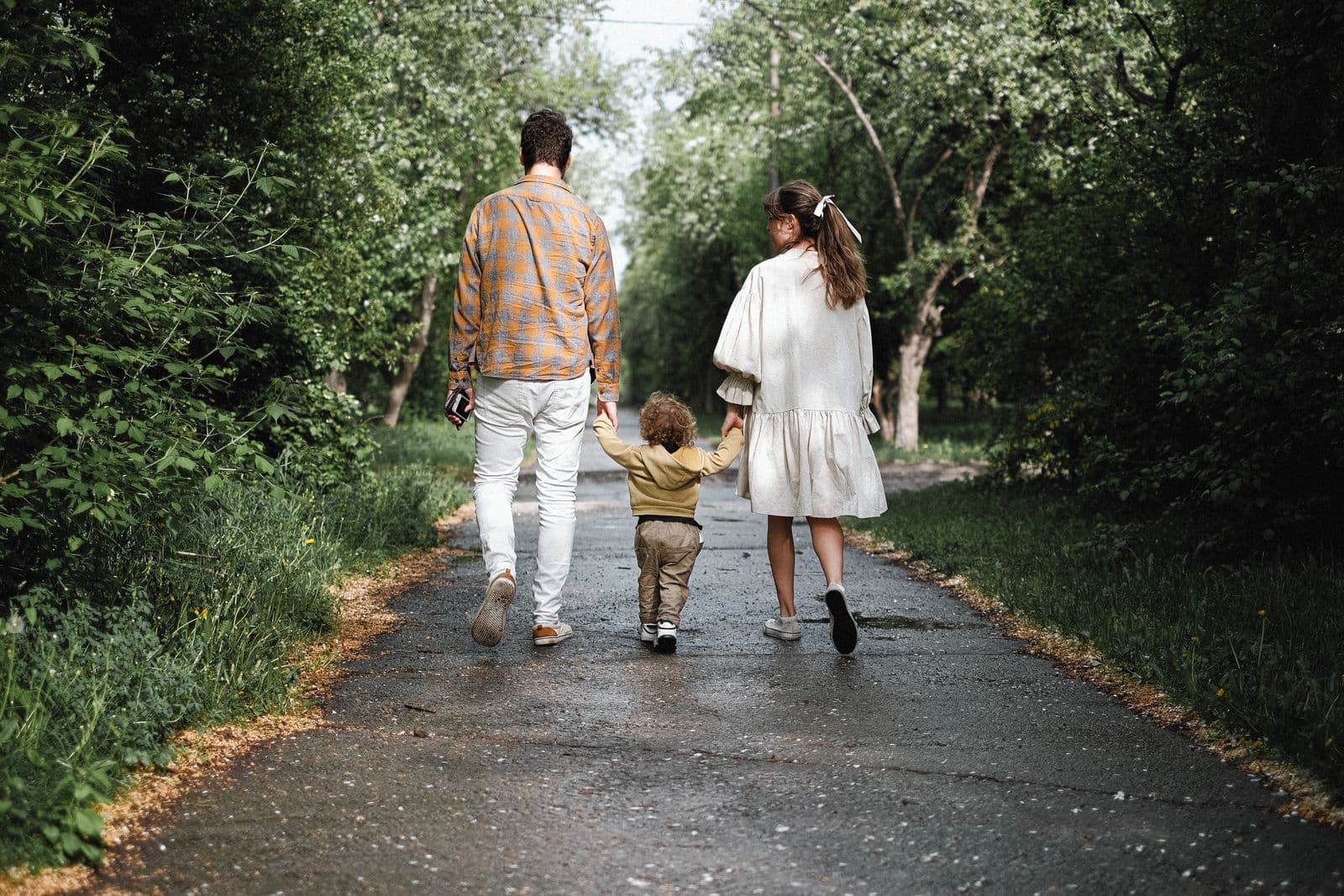 Un couple et un jeune enfant, vus de dos, marchent sur un chemin bordé d'arbres