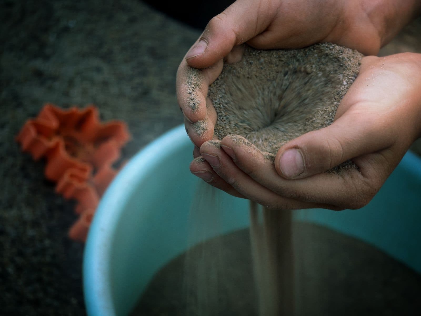 Les mains d'un enfant laissent couler du sable au-dessus d'un seau bleu