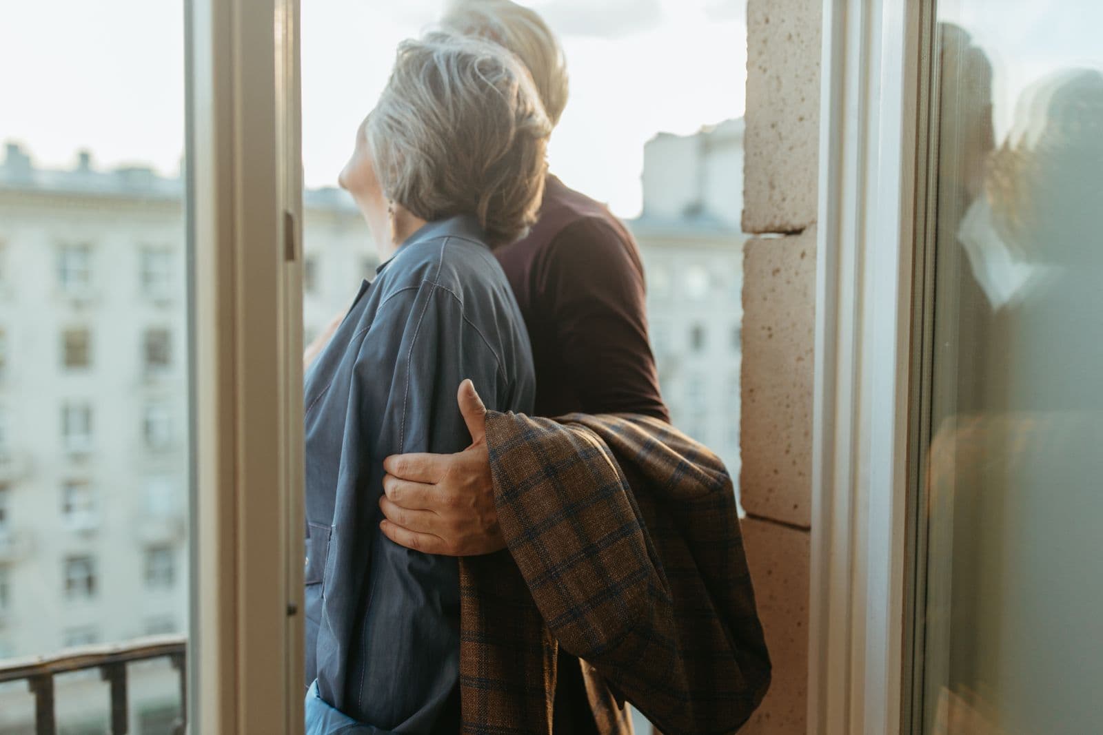 Un couple d'une soixantaine d'années enlacé sur un balcon, devant des immeubles