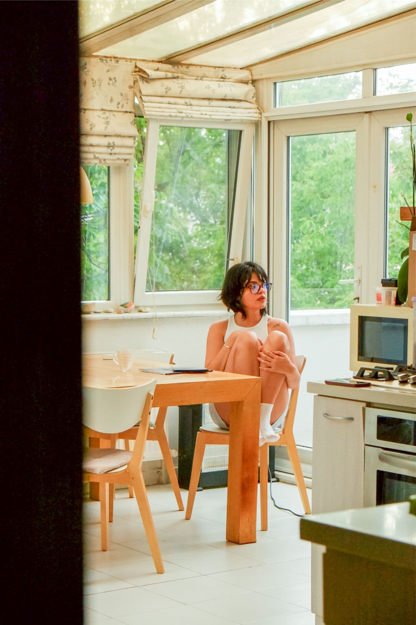 Une femme assise seule à une table de cuisine, dans une véranda baignée de soleil
