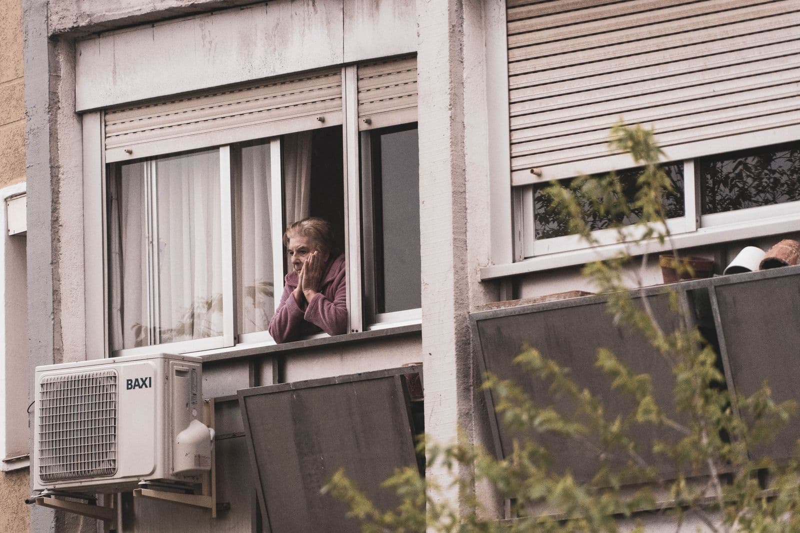 Une femme âgée regarde depuis la fenêtre ouverte de son appartement, dans un immeuble