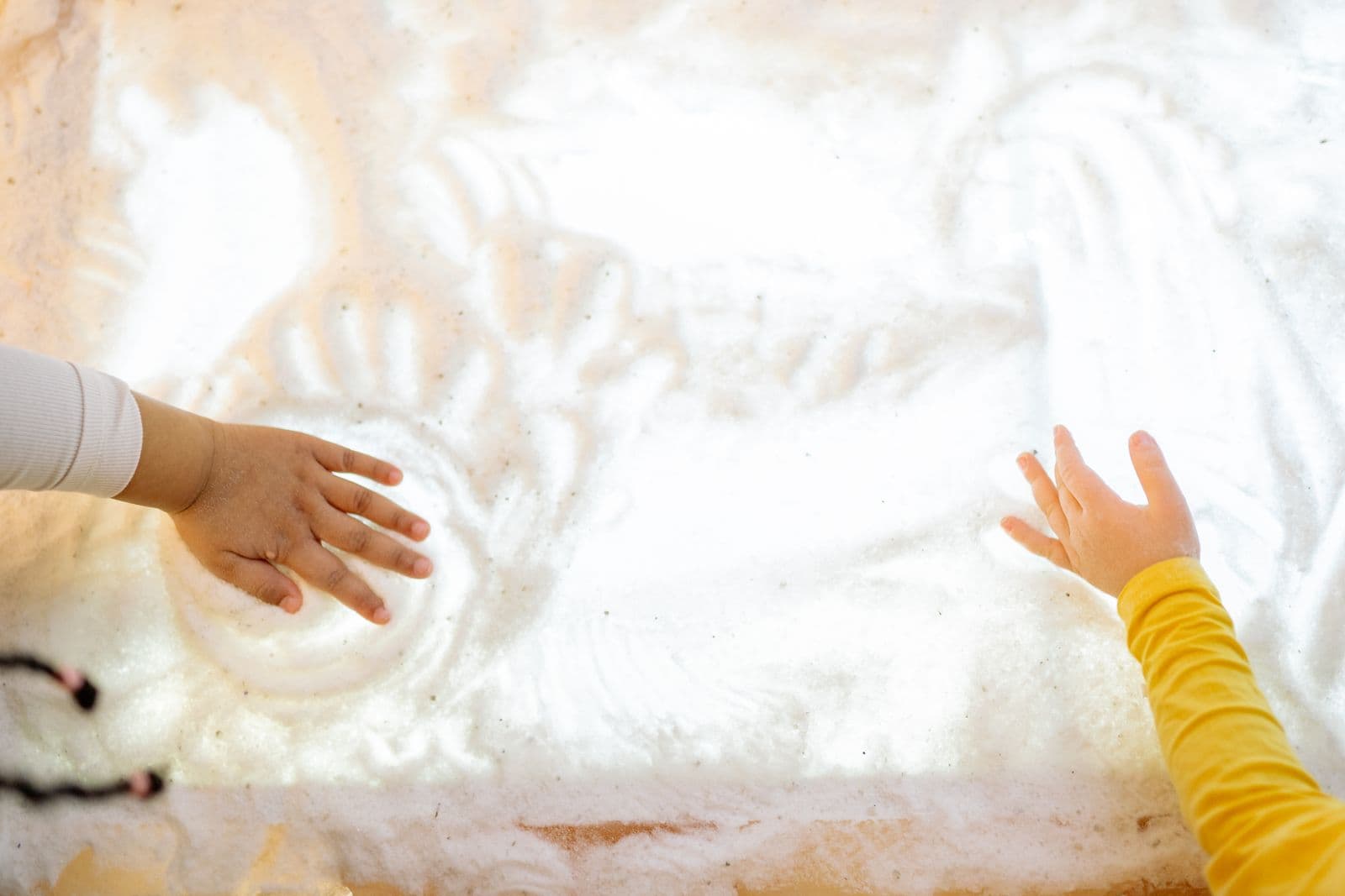 Deux mains d'enfants dessinent dans du sable sur une table lumineuse