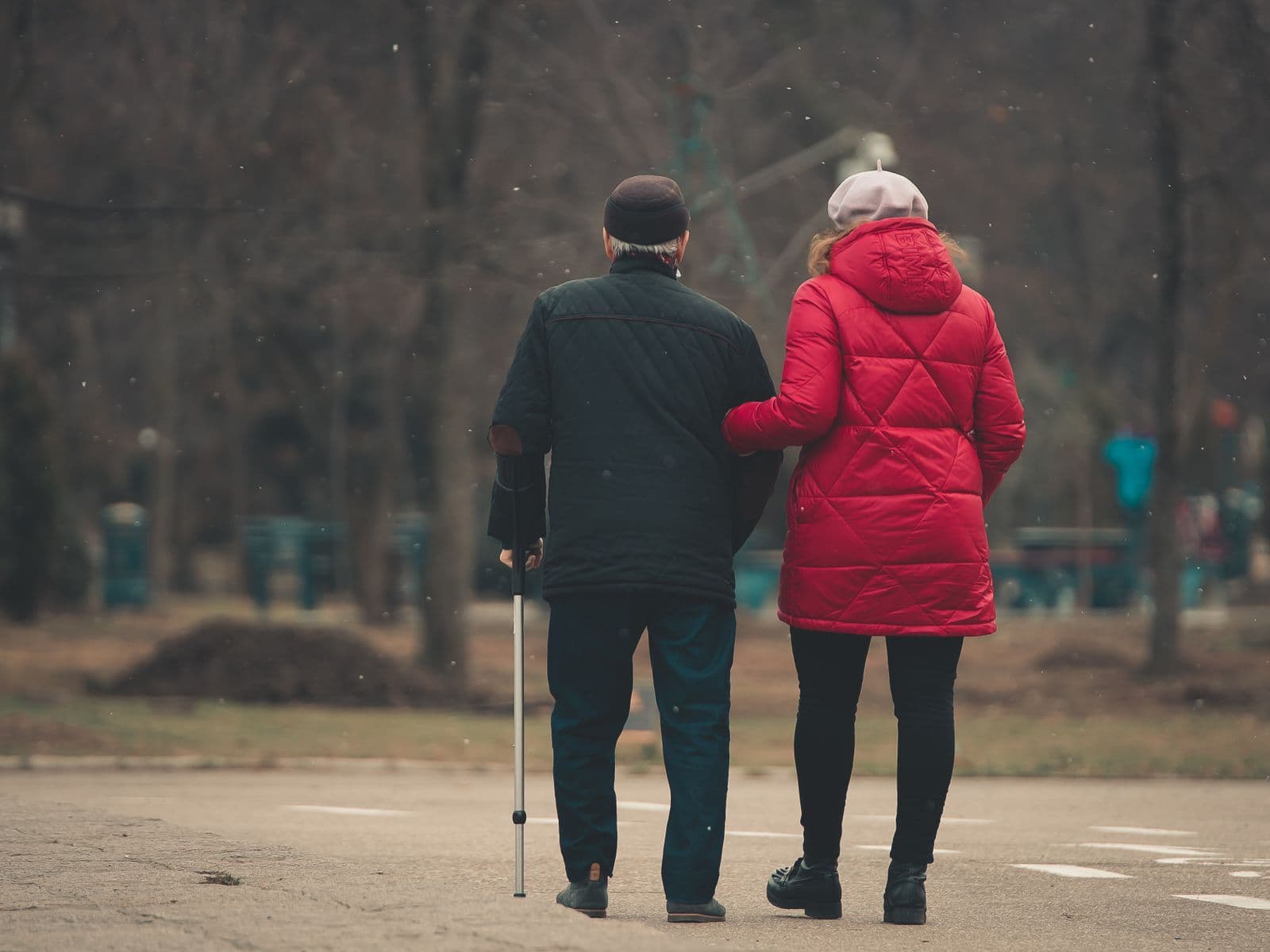Un couple âgé, vu de dos, marche bras dessus bras dessous dans un parc, l'homme s'appuie sur une canne