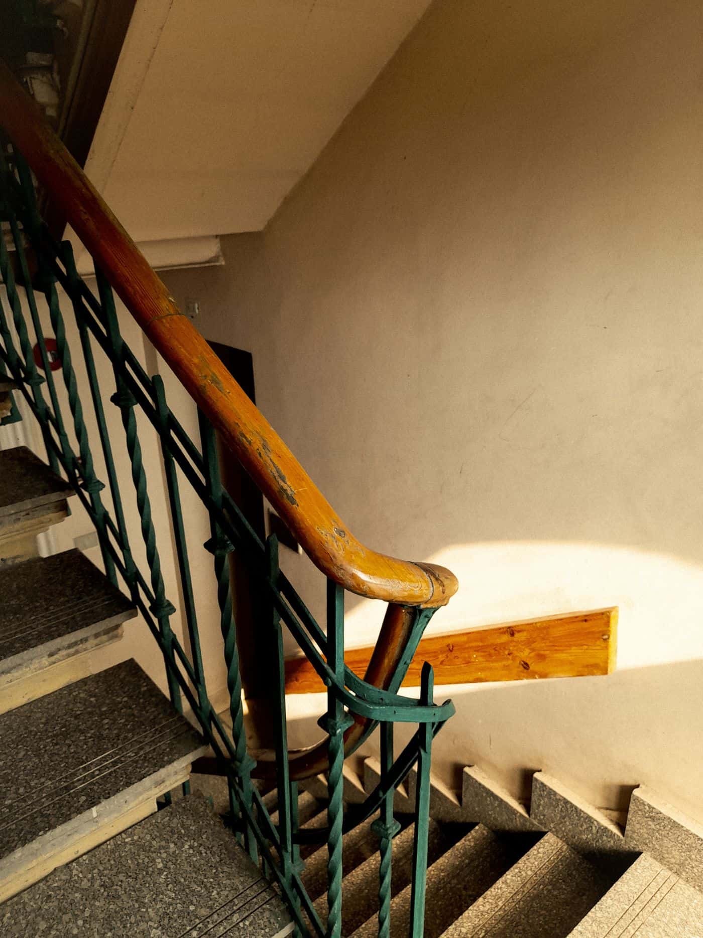 Un escalier d'immeuble avec une rampe en bois, éclairé par le soleil