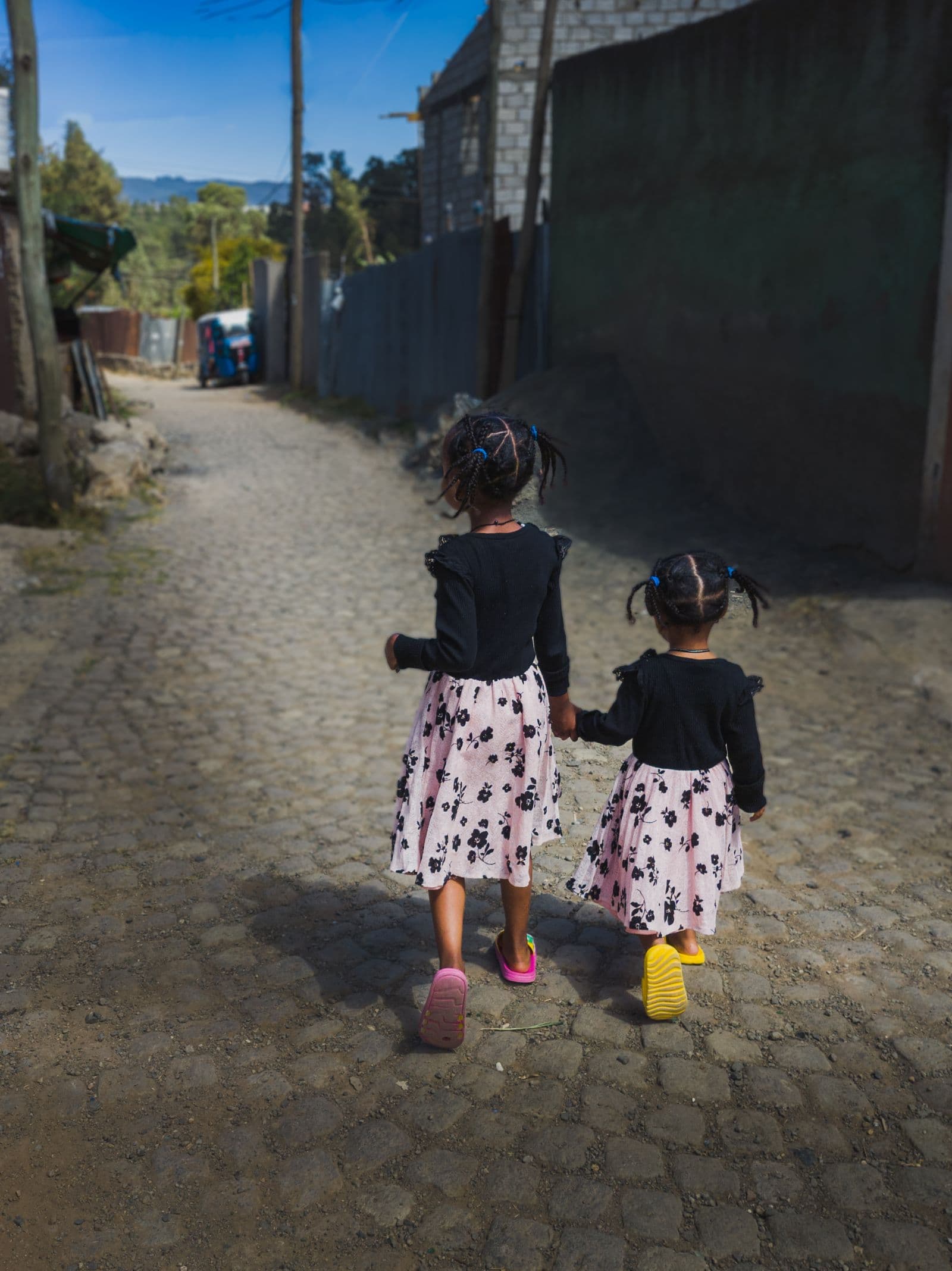 Deux petites filles, vues de dos, marchent main dans la main dans une ruelle pavée