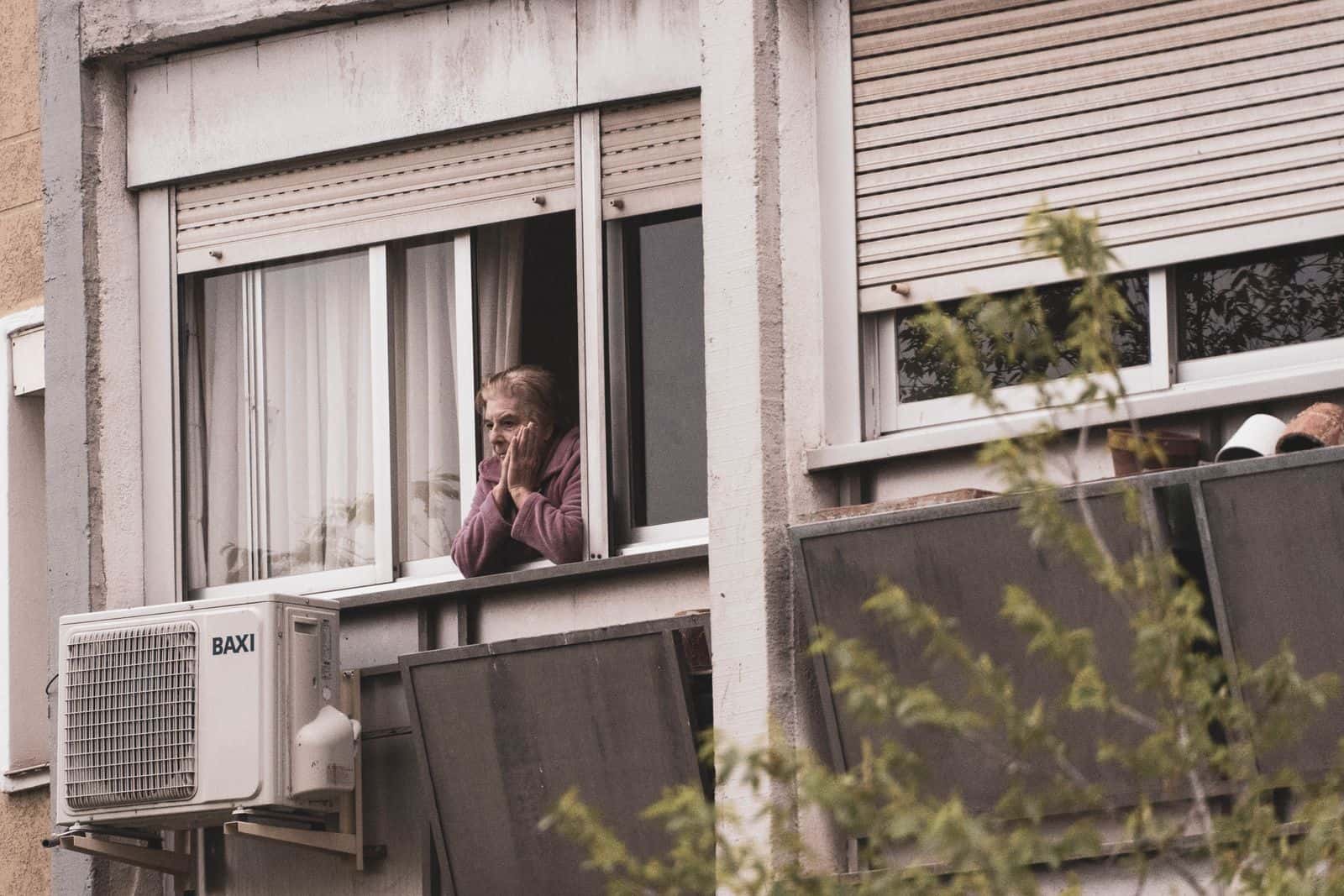 Une femme âgée regarde depuis la fenêtre ouverte de son appartement, dans un immeuble
