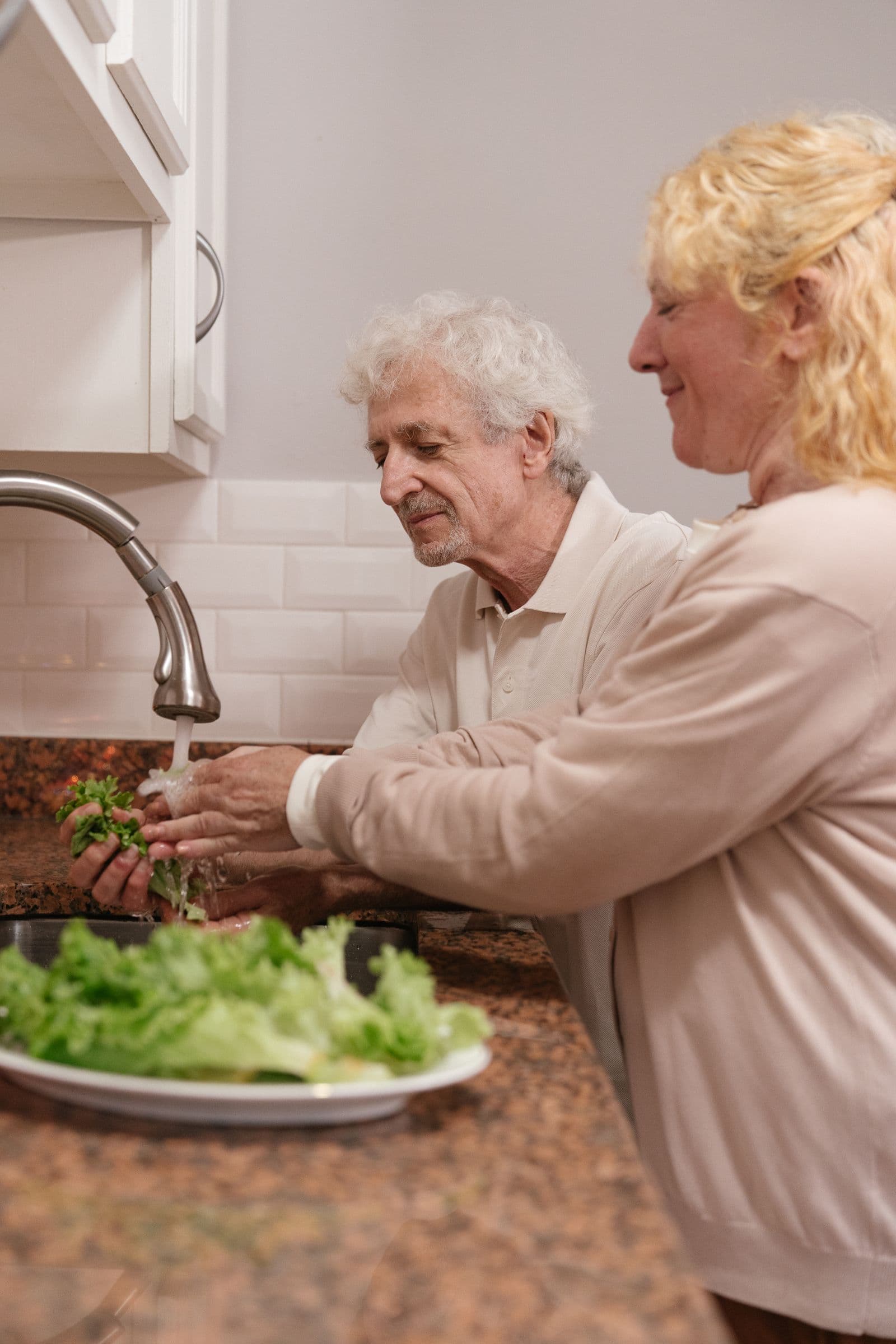 Un couple âgé lave de la salade dans une cuisine
