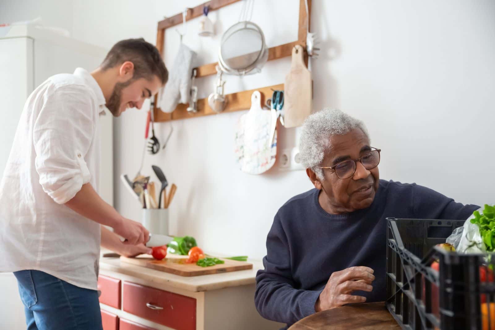 Un jeune homme prépare des légumes dans une cuisine tandis qu'un homme âgé assis à la table le regarde