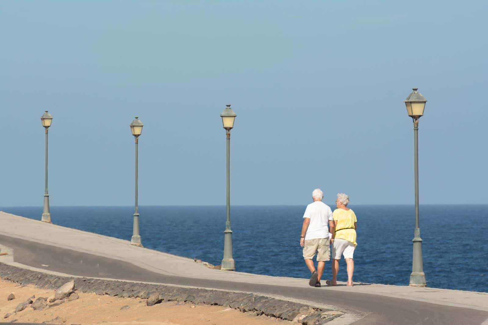 Un couple âgé marche sur une promenade de bord de mer bordée de lampadaires