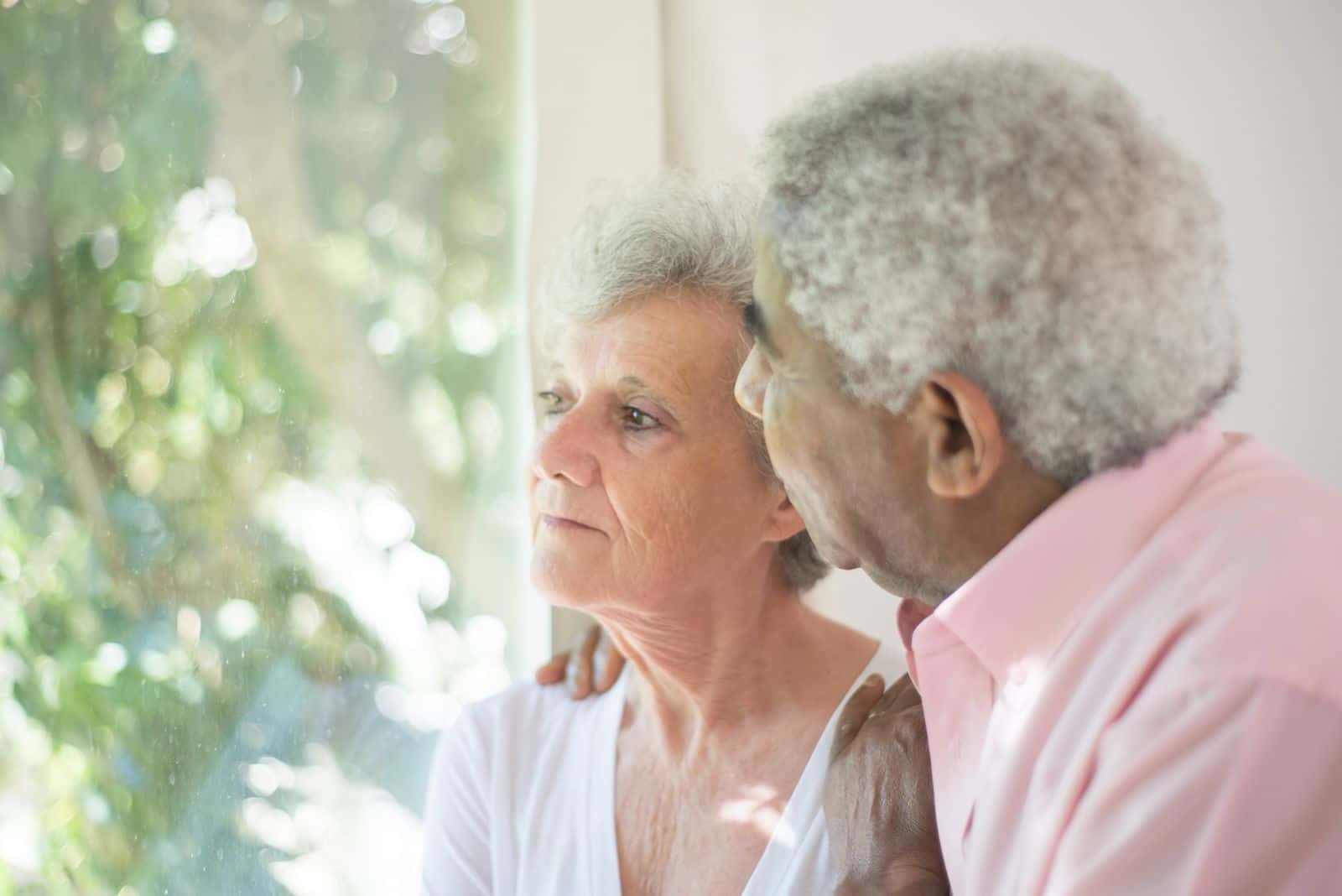 Un couple âgé se tient enlacé devant une fenêtre, en pleine lumière